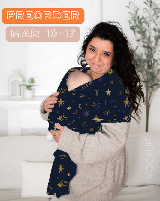 Woman holding a newborn in a bamboo stretchy baby carrier, the carrier is navy blue with a celestial hand-drawn pattern.