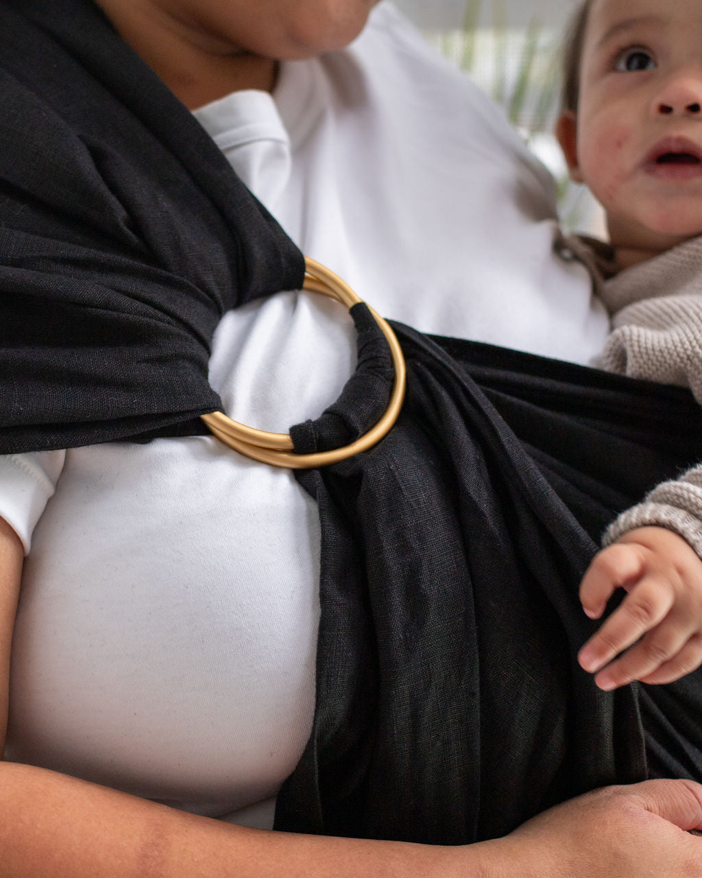 Person holding a baby in a black linen sling with a gold rings