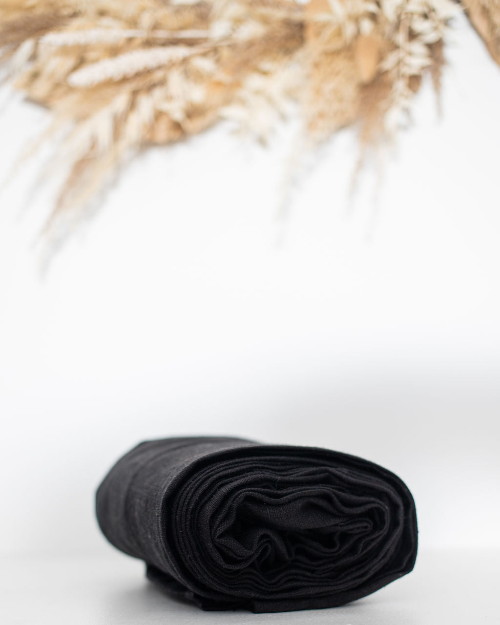 Rolled black linen ring sling on a white surface with dried plants in the background