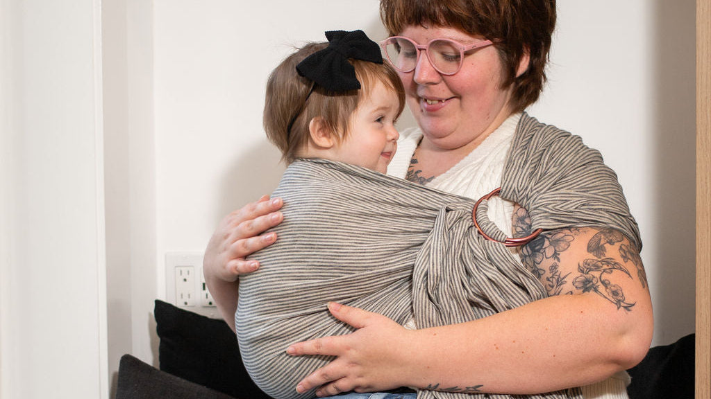Woman holding a child wrapped in a sling on a couch