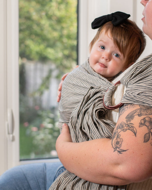 Baby wrapped in a striped ring sling being held by a person with tattoos,