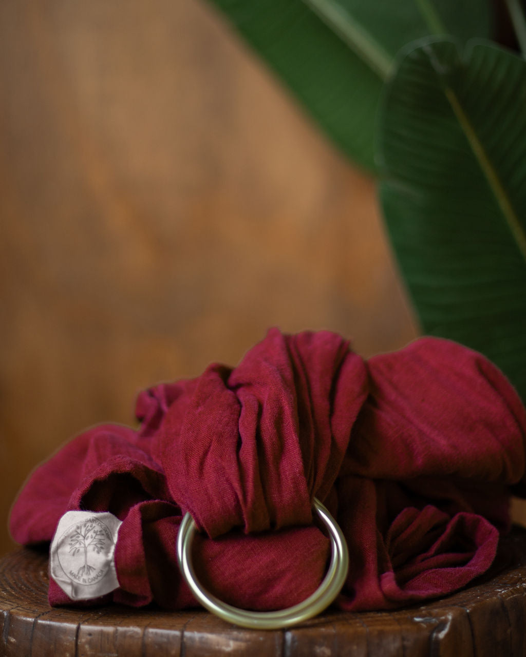 Bala (cranberry Red) ring sling baby carrier fall product photo on a stump with a blurred natural background