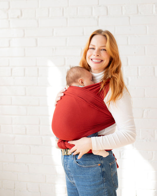 Mom wearing ginger/red/orange stretch wrap baby carrier with infant