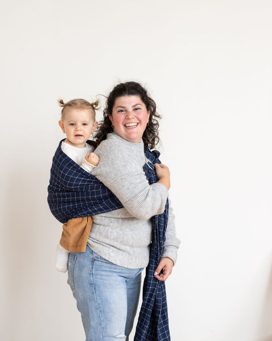 mom wearing a toddler in back carry with a blue checkered ring sling