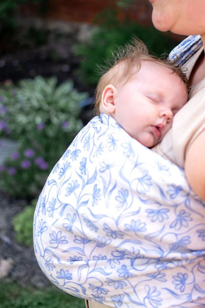 Baby sleeping in a blue and white floral baby carrier with a blurred outdoor background