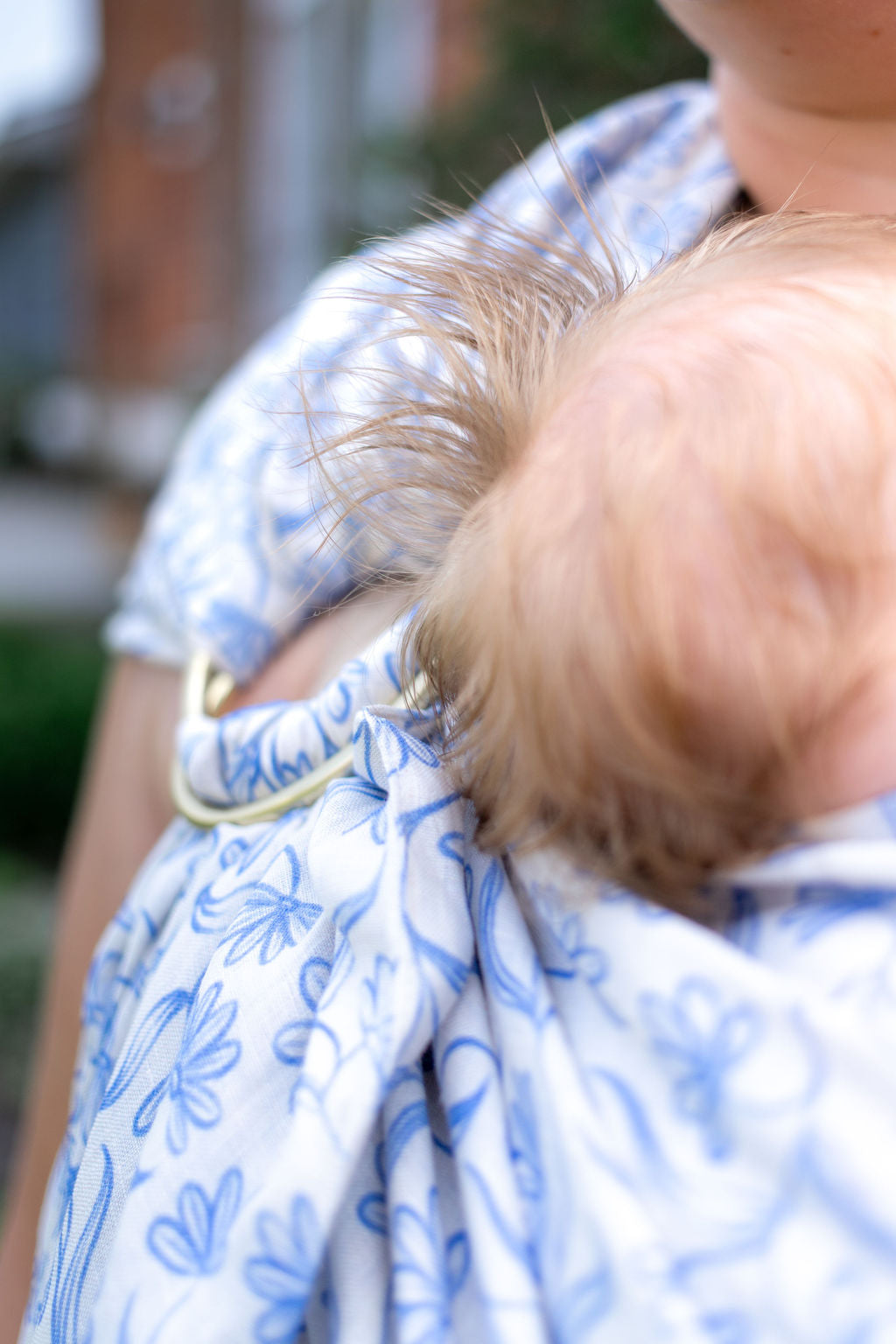 Person wearing a baby in a blue floral sling outdoors