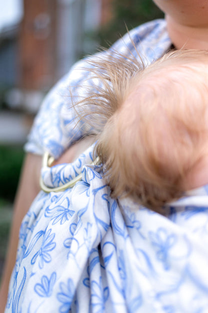 Person wearing a baby in a blue floral sling outdoors