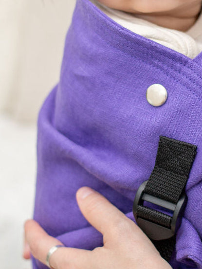 Woman holding a child in a purple baby carrier against a white background