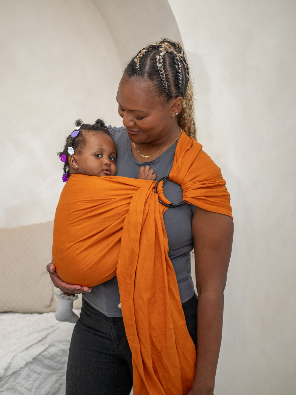 Woman holding a baby in an orange ring sling against a plain background