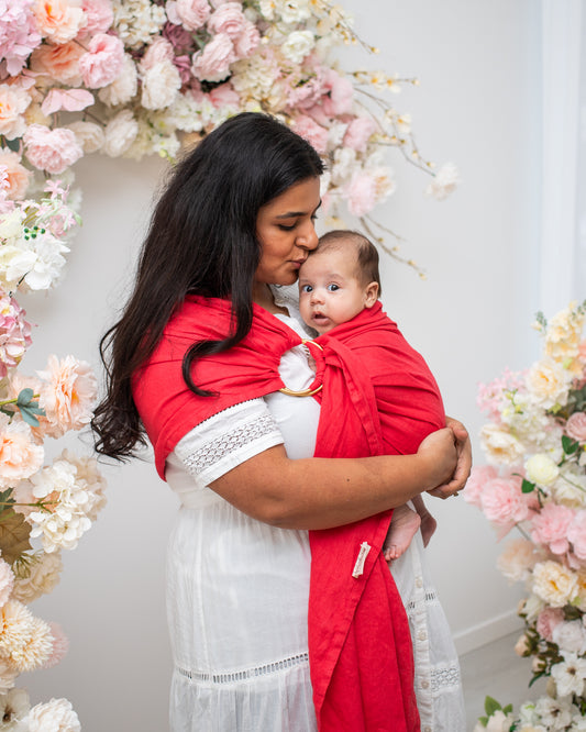 mom kissing baby's head while using a watermelon red linen ring sling