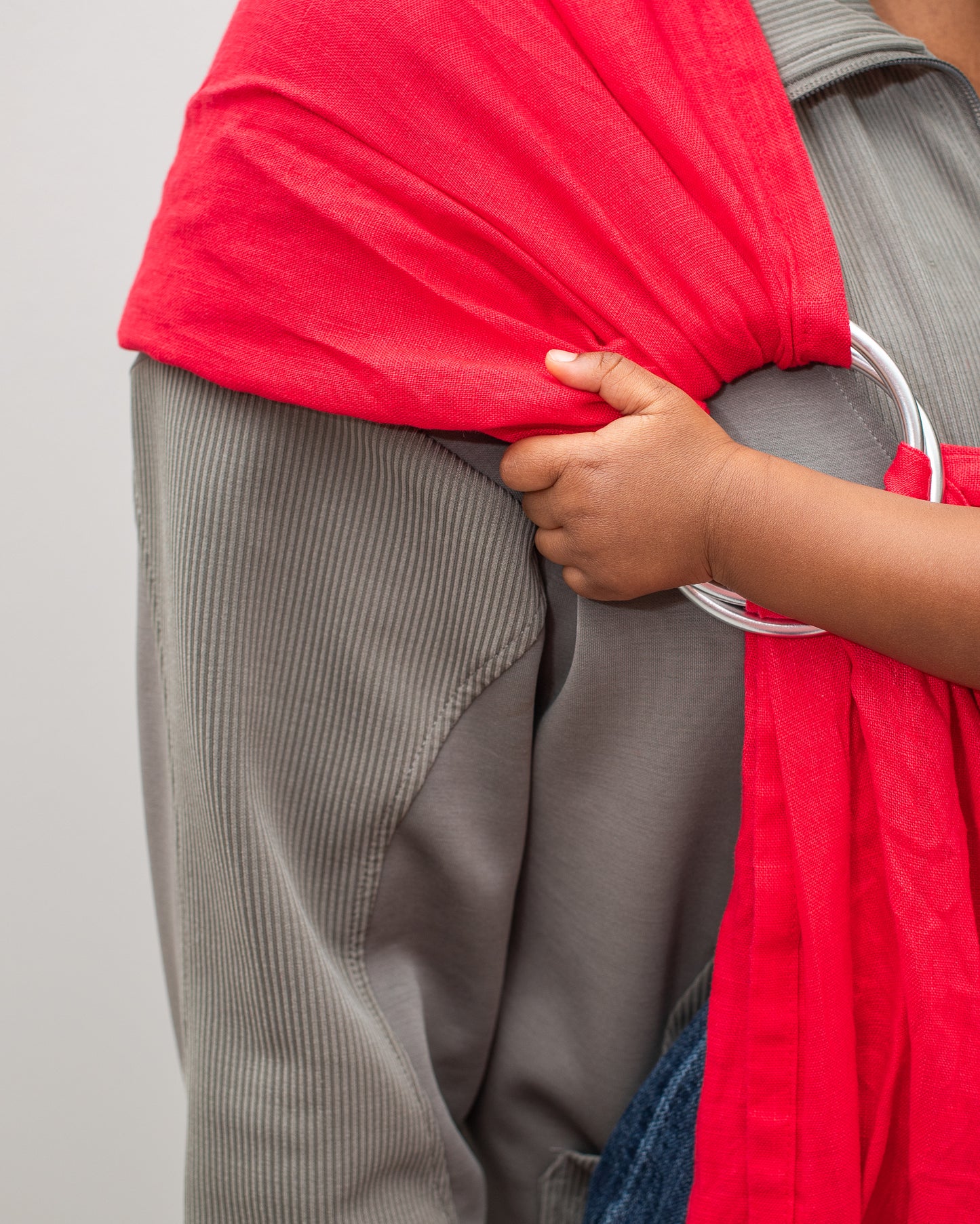 close up of toddler hand holding onto the rings of a watermelon red linen ring sling carrier