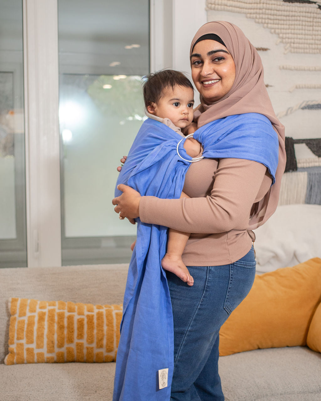 Mom wearing a baby in a blue coloured sling in a living room 