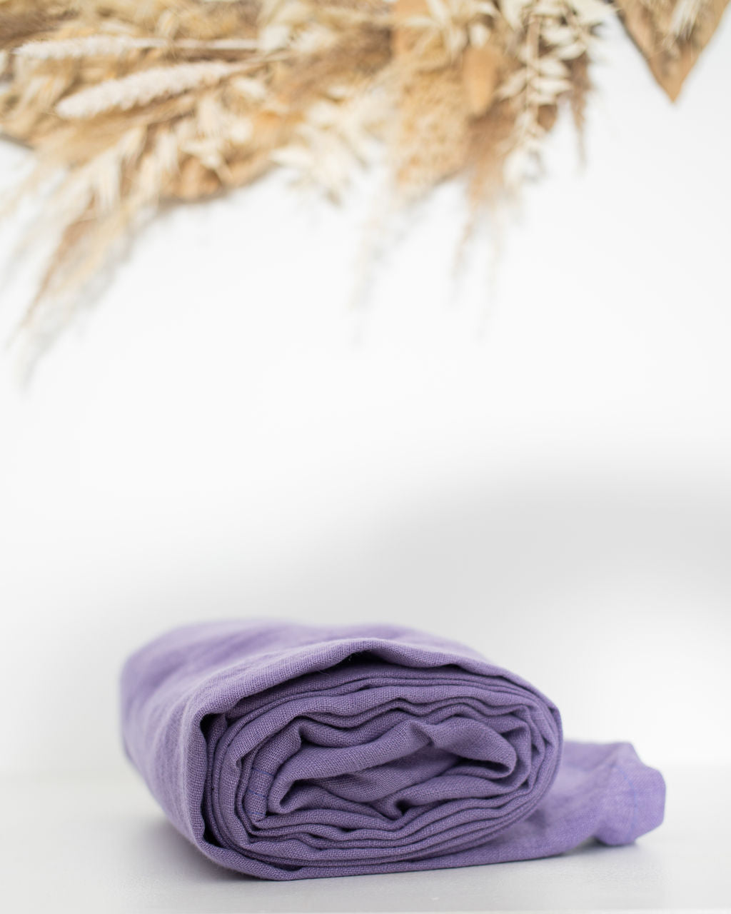Folded purple linen ring sling on a white background with dried plants 
