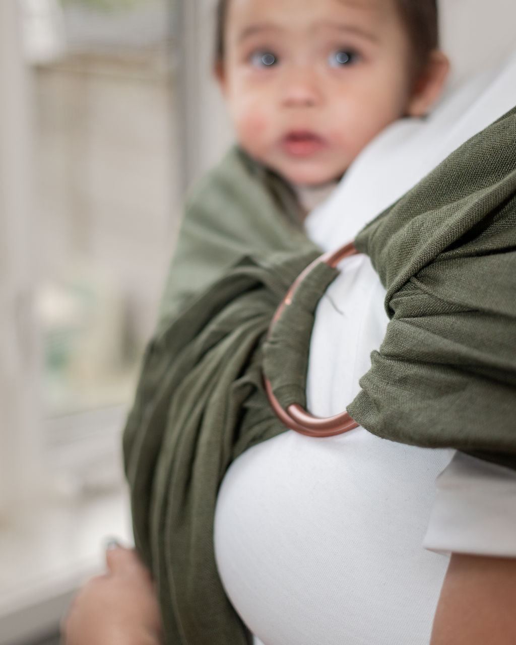 Baby in a green linen ring sling baby carrier with a blurred background