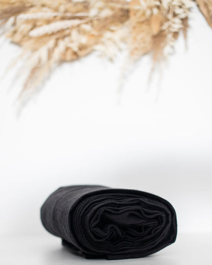 Rolled black linen ring sling on a white surface with dried plants in the background