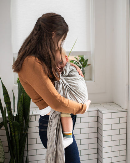 Woman feeding baby in a ring sling carrier in a home setting