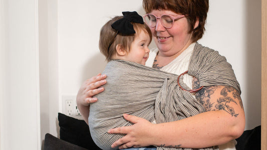 Woman holding a child wrapped in a sling on a couch