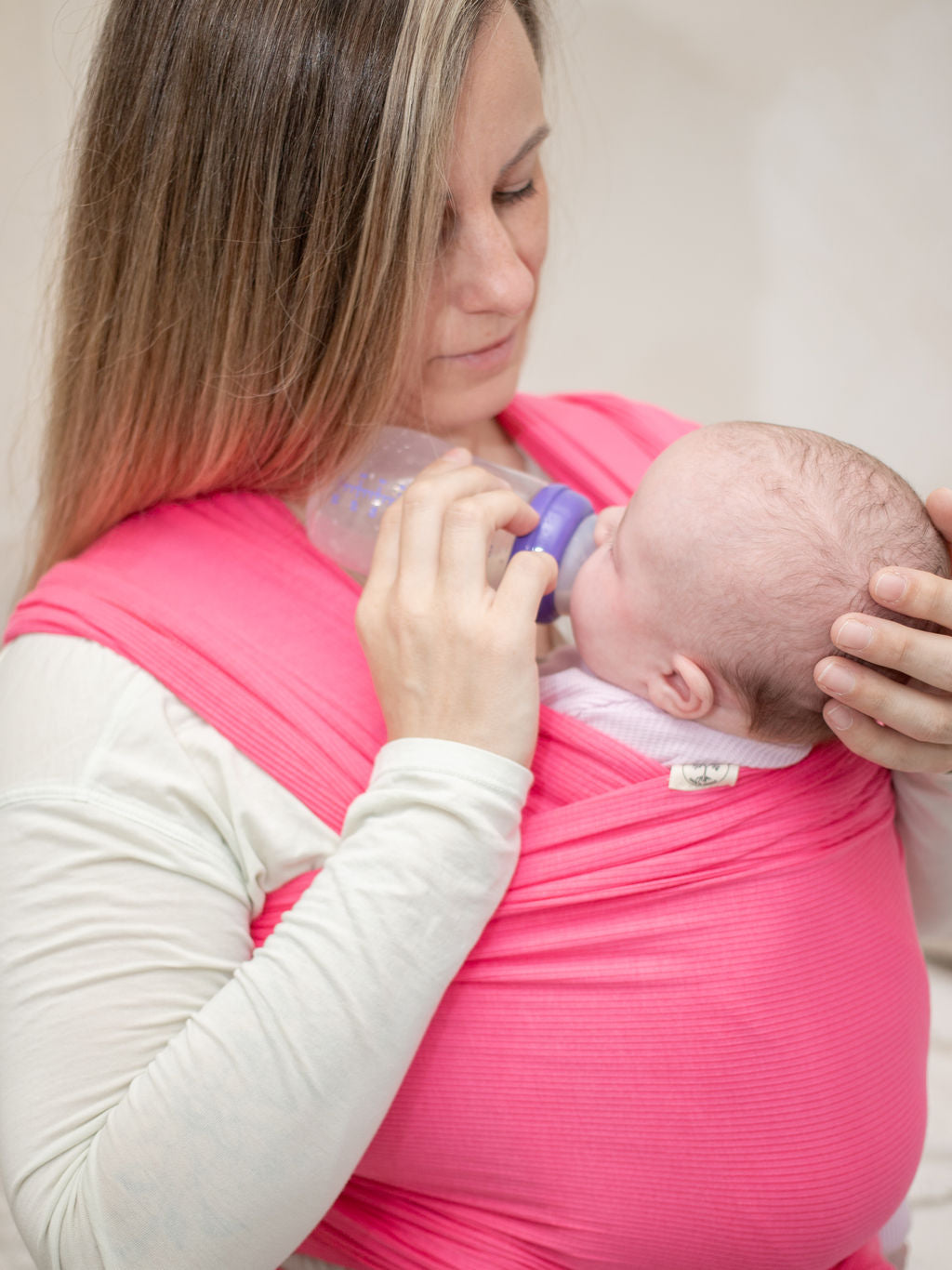 Mom bottle feeding baby in stretchy wrap carrier