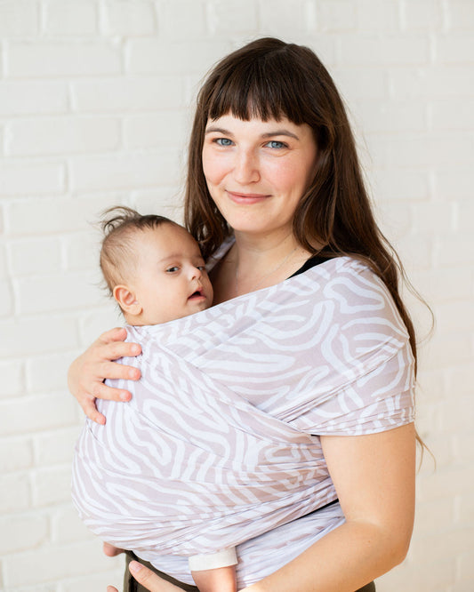 Woman wearing a baby in a beige and white stretch wrap 