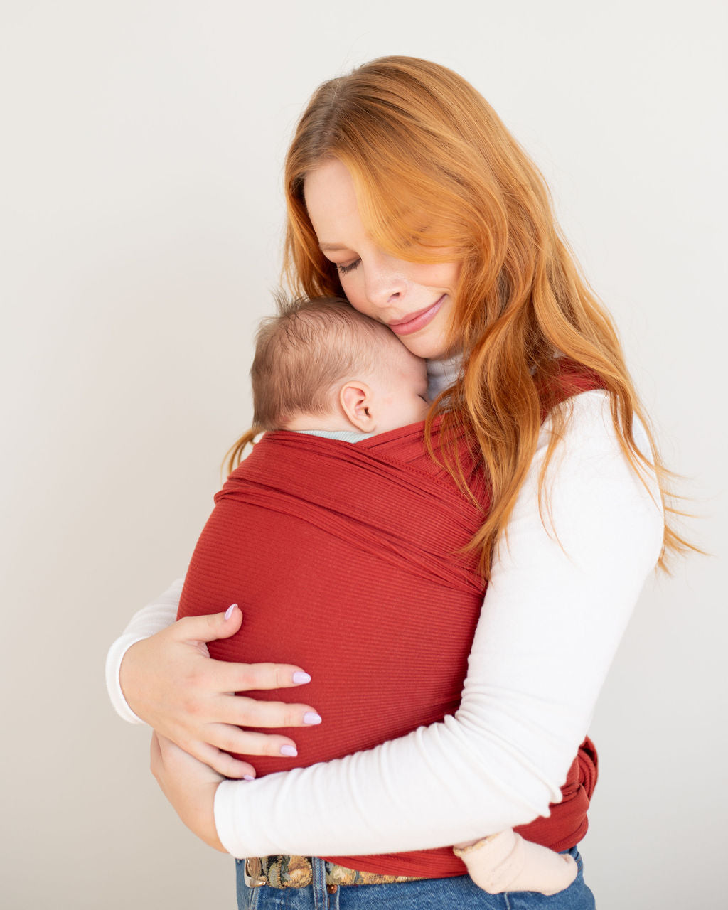 Woman holding a baby wrapped in a red / orange stretchy carrier 