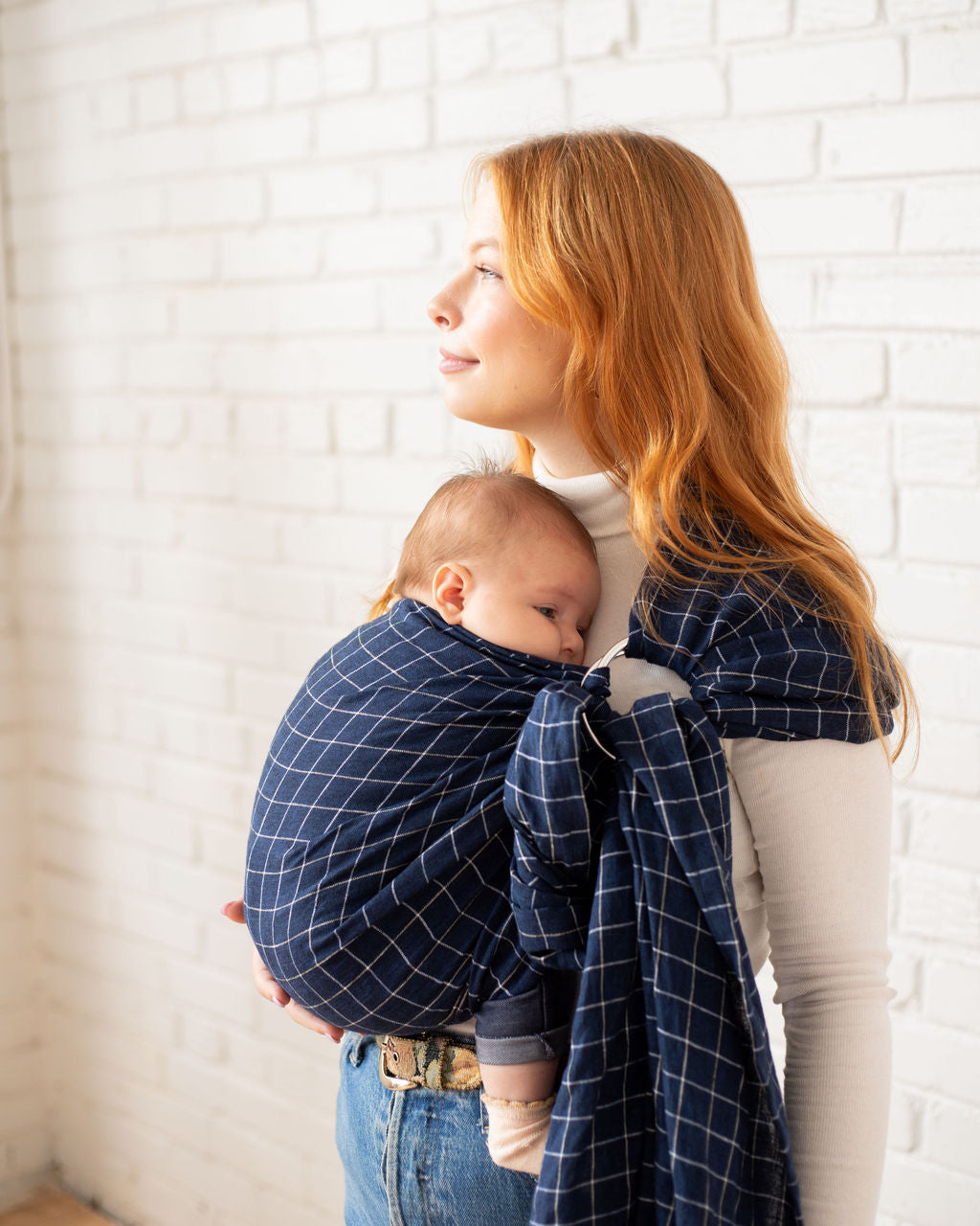Woman holding a baby wrapped in a blue checkered ring sling 