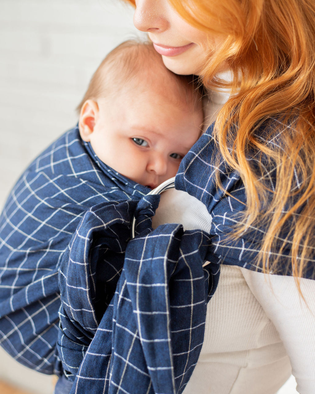 close up of mother wearing sleepy baby in navy blue checkered ring sling baby carrier