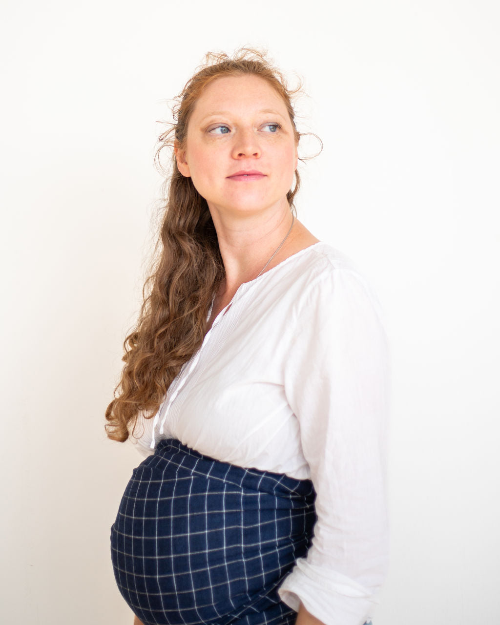 pregnant Woman wrapping belly for support with a blue plaid ring sling