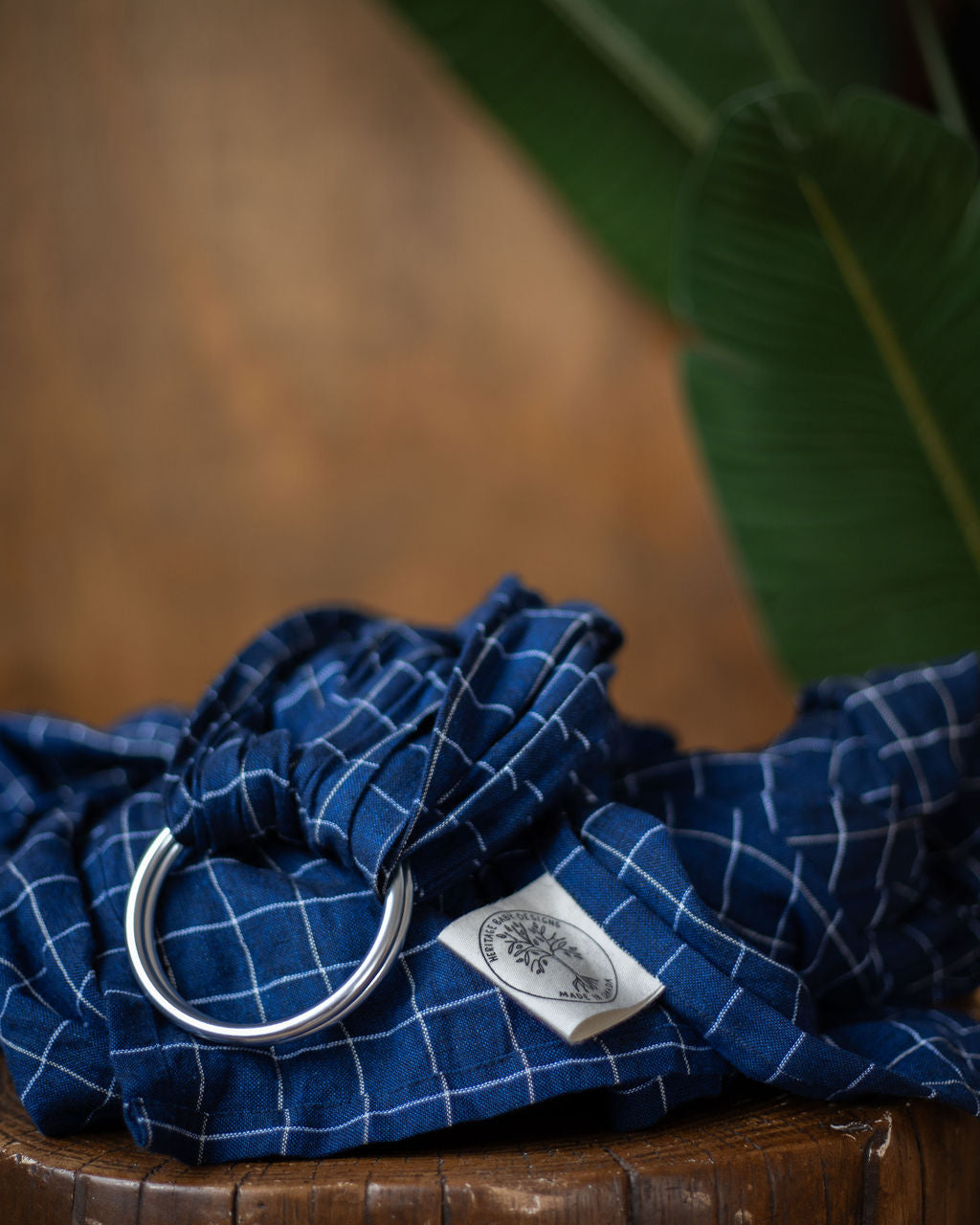 Blue checkered ring sling fall product photo on a stump with a blurred green leaf in the background.