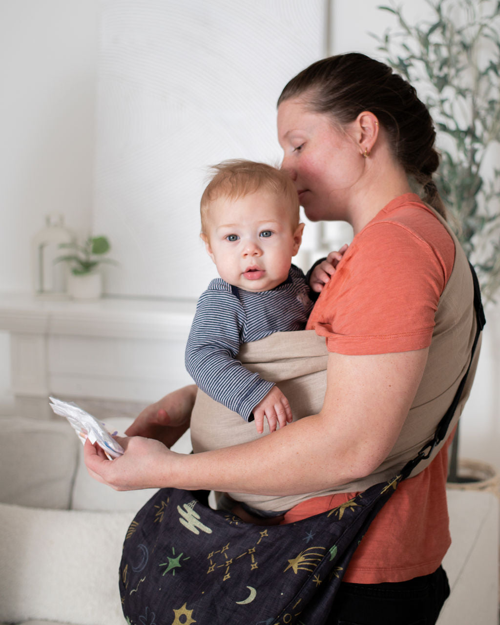 Woman holding a baby in a sling while wearing a linen crescent bag 