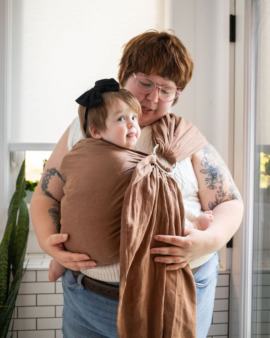 plus sized woman wearing a baby in a brown ring sling baby carrier 