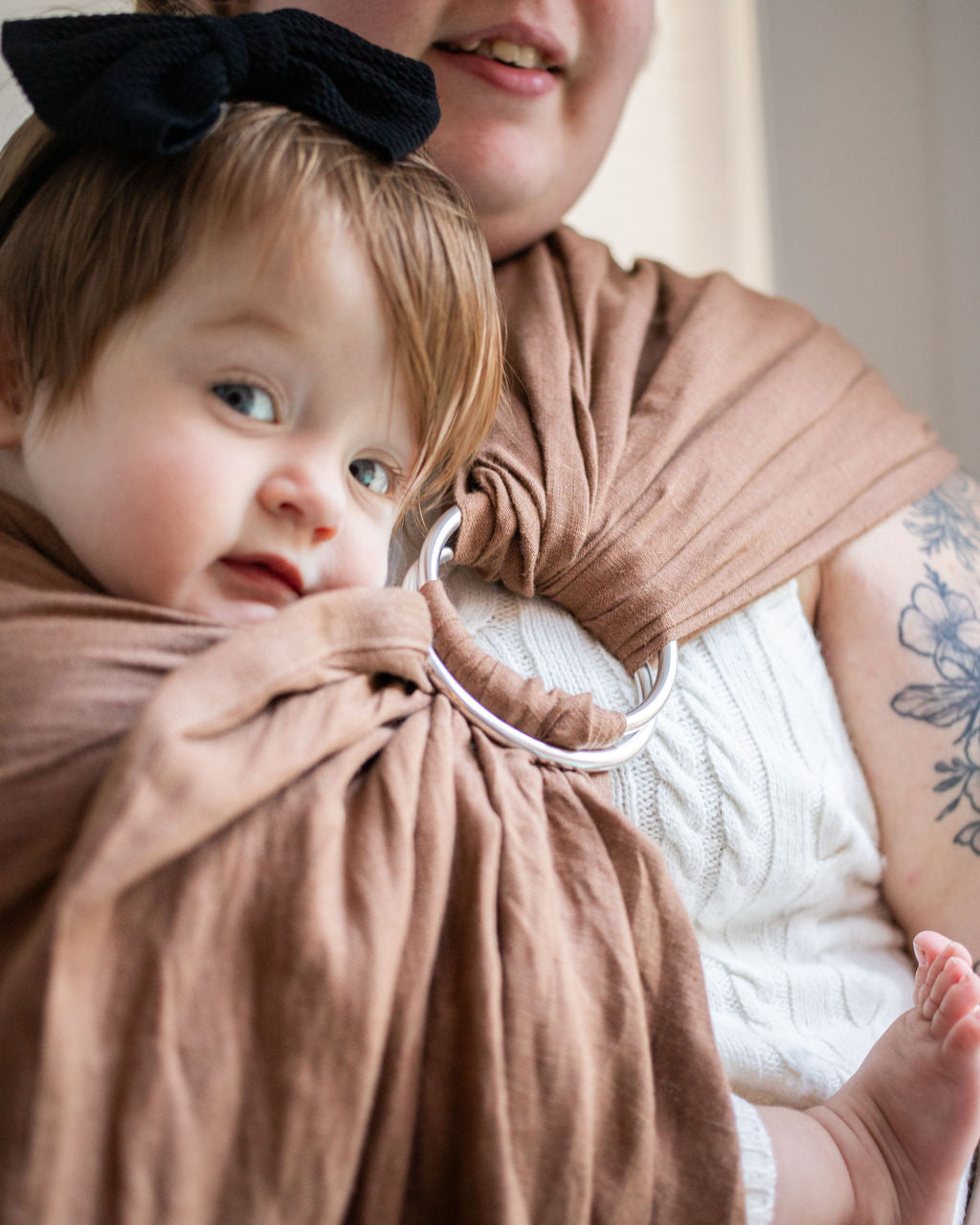 Woman holding a baby wrapped in a brown sling.