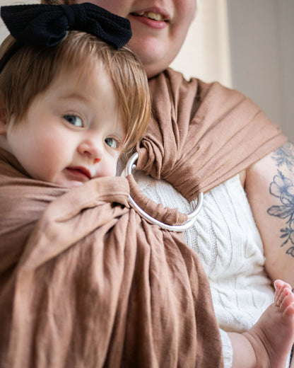Woman holding a baby wrapped in a brown sling.